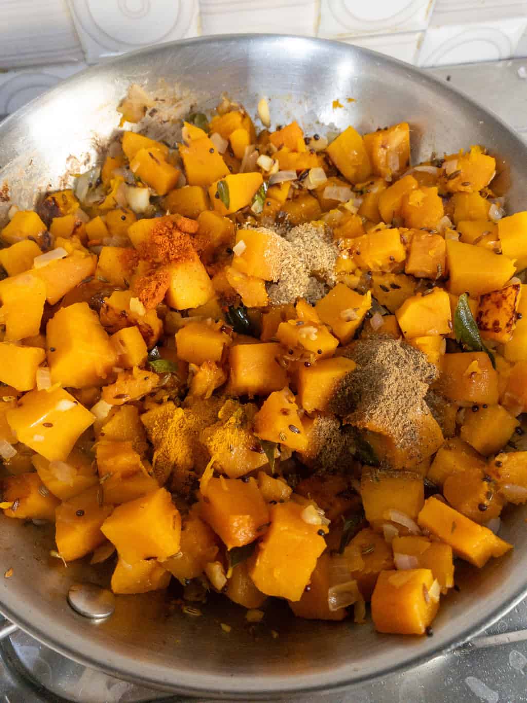 Cooked pumpkin cubes mixed with turmeric, coriander, chili, and garam masala powders while making Indian pumpkin stir fry.