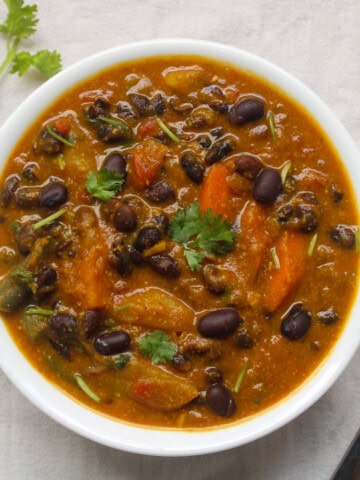 Top view of vegan pumpkin black bean vegetable curry served in a white bowl with cilantro garnish.