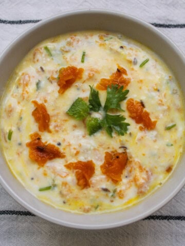 Overhead shot of pumpkin raita showing its creamy texture with grated pumpkin, herbs, and a cilantro garnish.