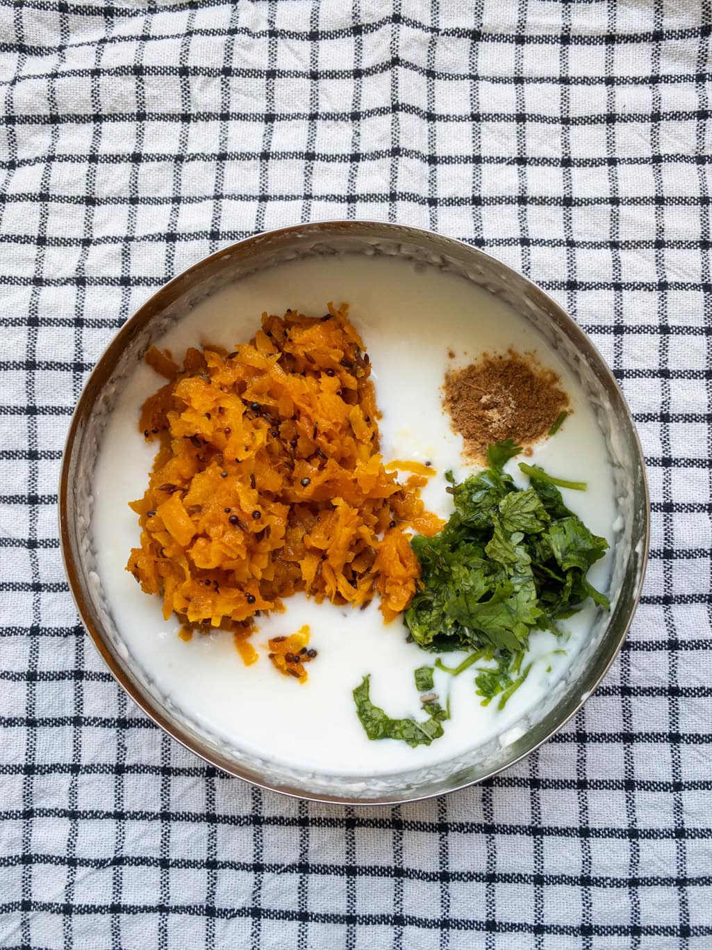 Curd mixed with cooked grated pumpkin, dry ginger powder, and chopped coriander before stirring to make pumpkin raita.