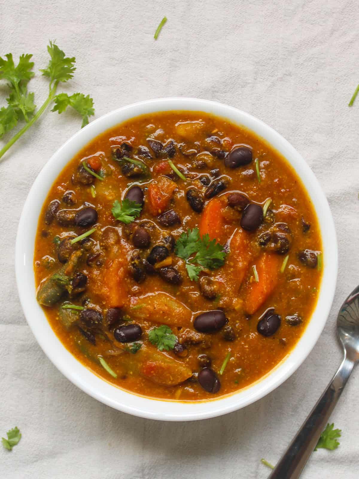 Overhead shot of pumpkin purรฉe black bean curry with carrots and beans, garnished with cilantro.