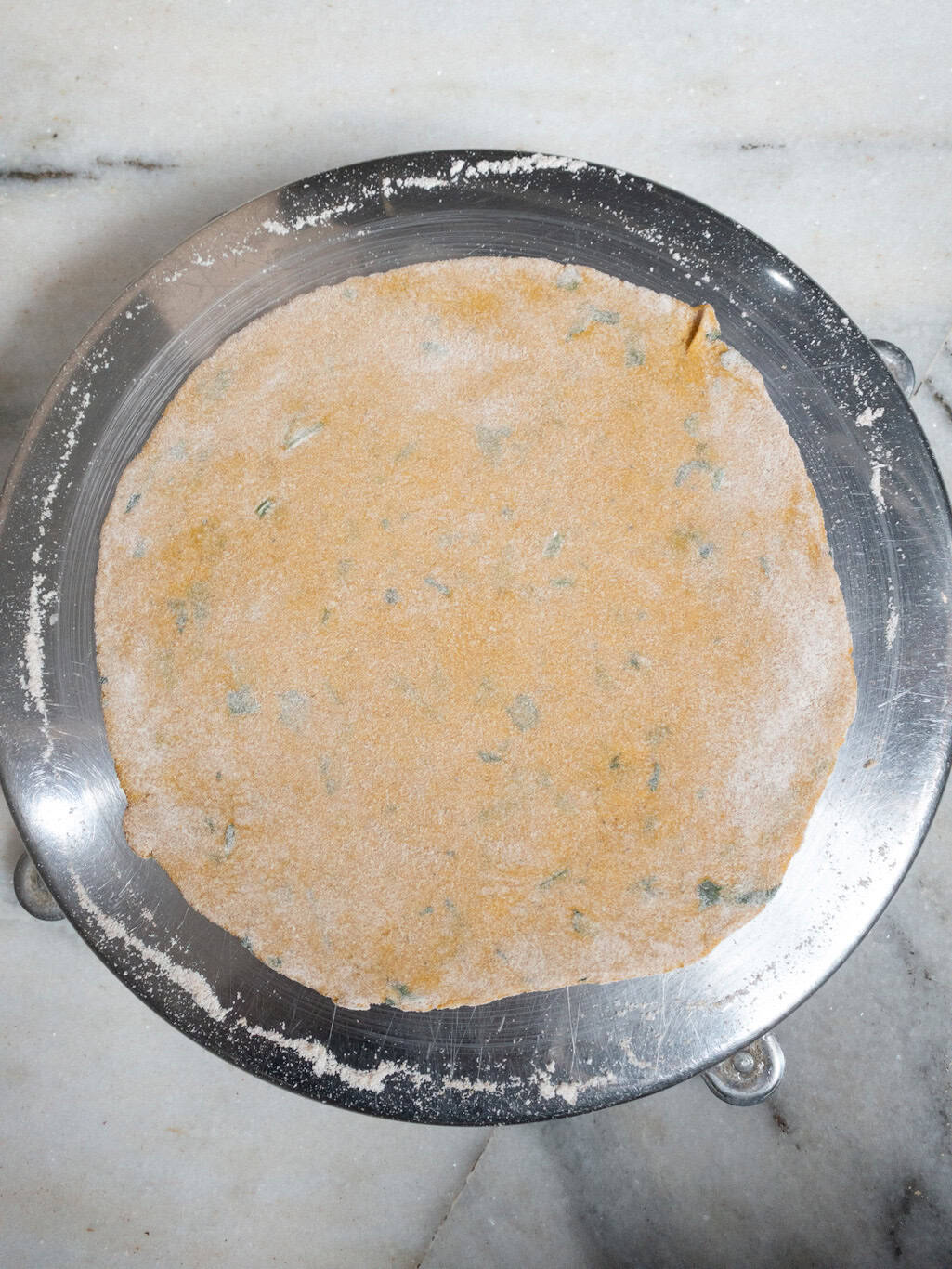 A rolled pumpkin paratha dough circle dusted with flour on a rolling board.