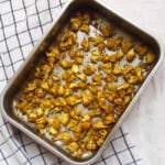 A tray of Indian spiced roasted cauliflower placed on a checkered kitchen towel, showing evenly browned, crisp florets.