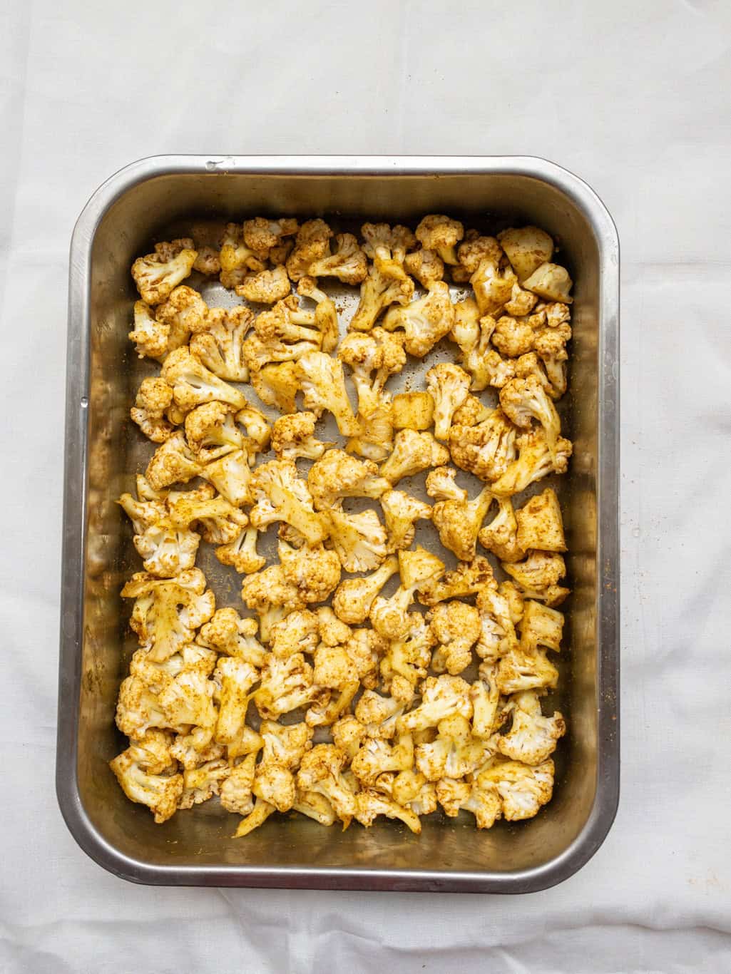 Cauliflower florets evenly coated with oil and spices, ready to be placed in the oven for roasting.