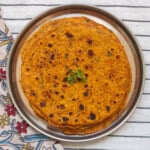 Stack of cooked pumpkin parathas on a steel plate, garnished with fresh cilantro.