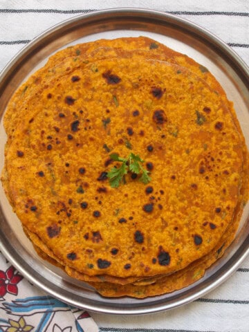 Stack of cooked pumpkin parathas on a steel plate, garnished with fresh cilantro.