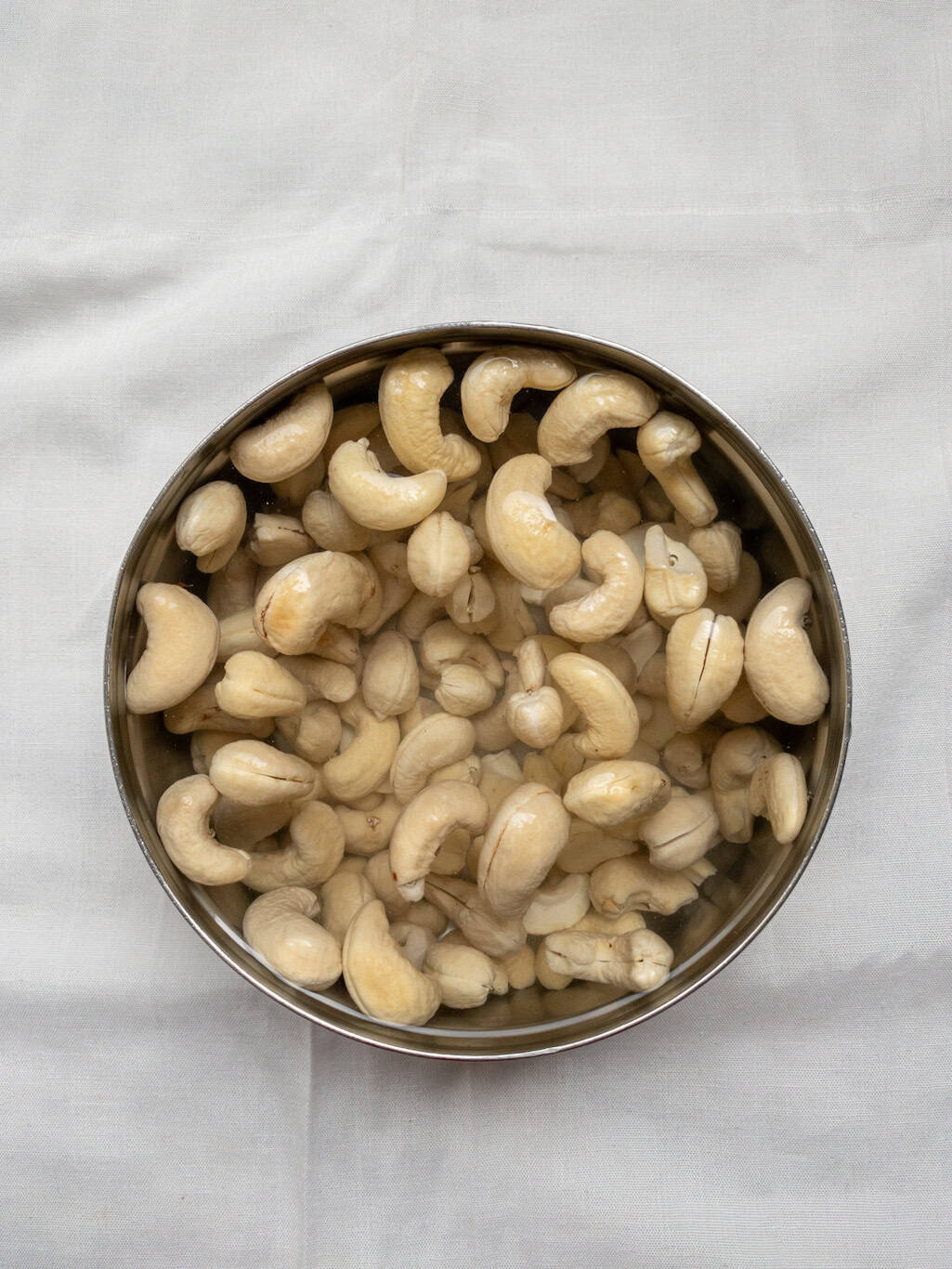 Raw cashews soaked in water in a steel bowl.