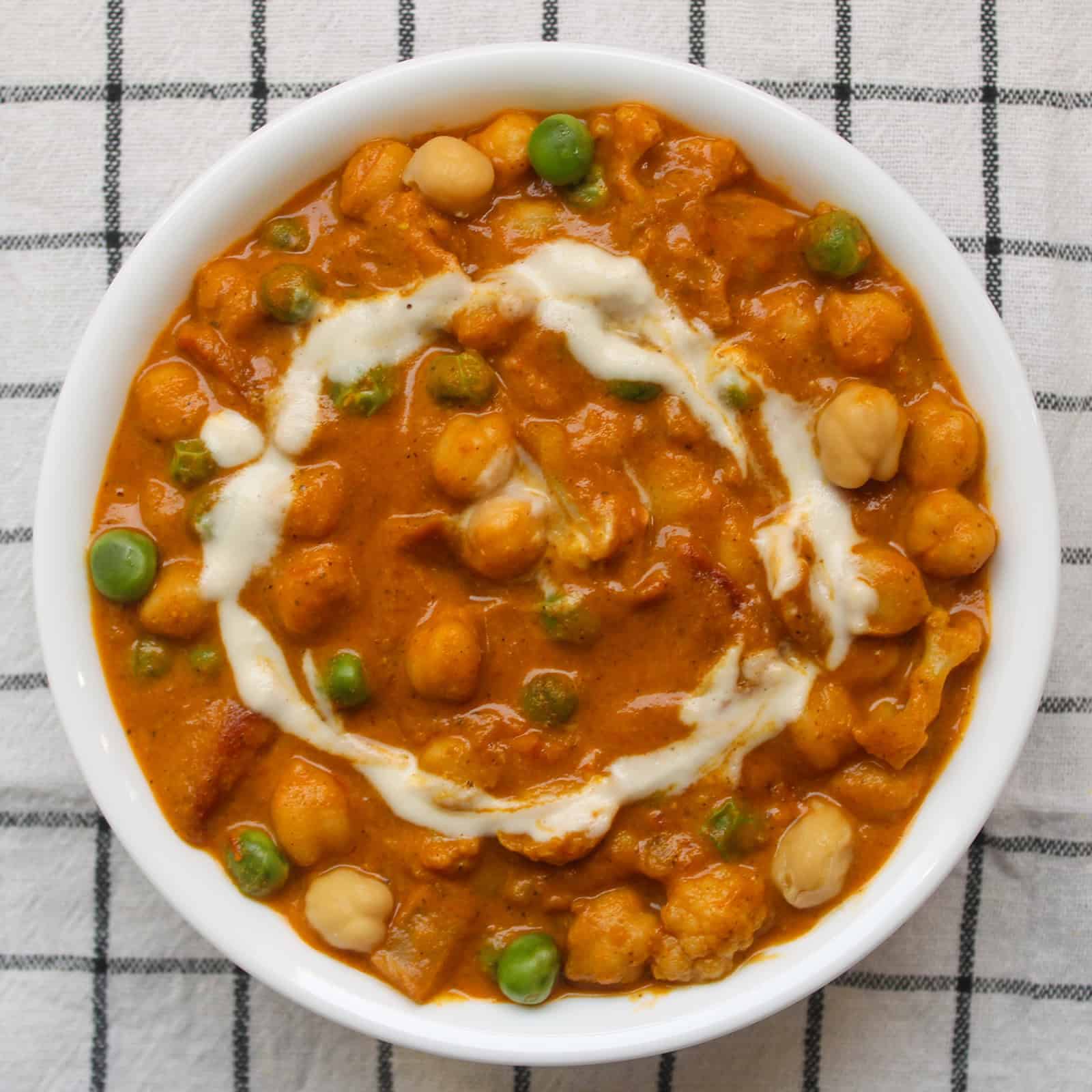 Chickpea tikka masala garnished with cream and green peas.