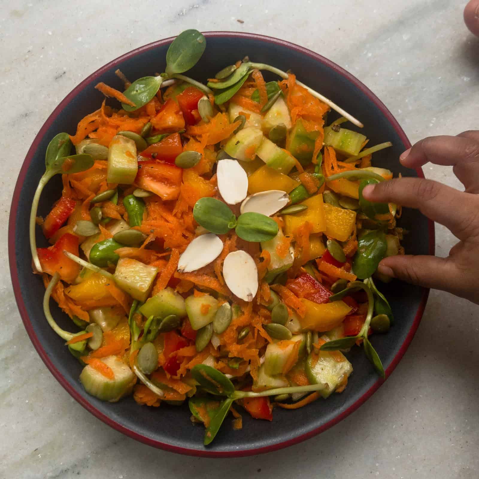 Fresh vegetable salad served in a bowl with sunflower sprouts, pumpkin seeds, and almonds.