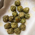 Baked spinach balls with lightly crisp edges resting on parchment paper.