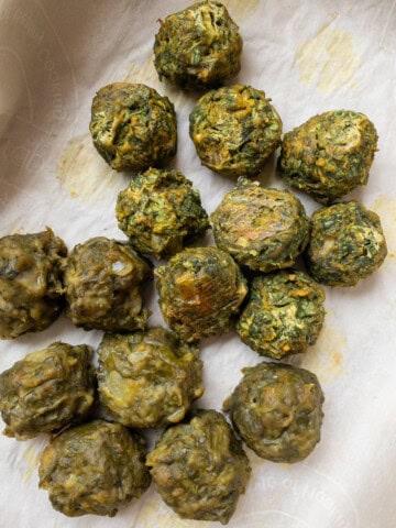 Baked spinach balls with lightly crisp edges resting on parchment paper.
