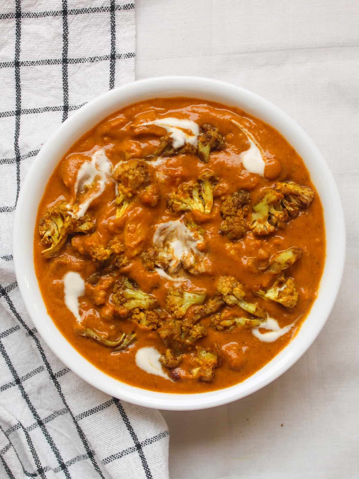 Creamy cauliflower tikka masala served in a white bowl, topped with roasted cauliflower and gentle swirls of cashew cream.