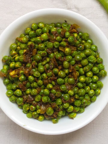 Indian spiced sautéed green peas served warm in a white bowl.