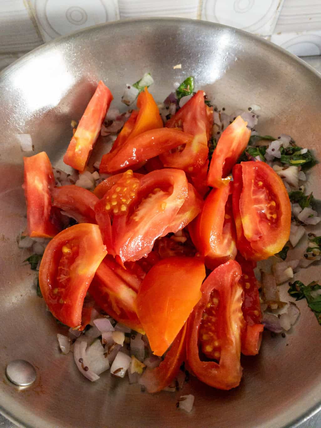 Fresh chopped tomatoes added to sautéed onions and tempering spices in a pan.