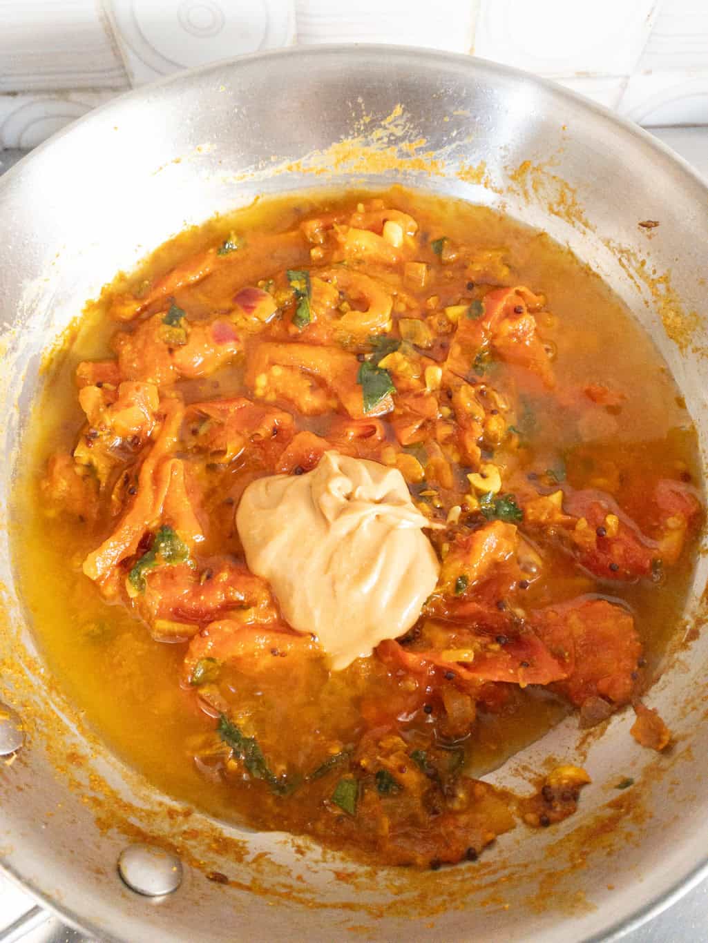 Spoonful of nut butter added to tomato curry to balance tanginess without cream.
