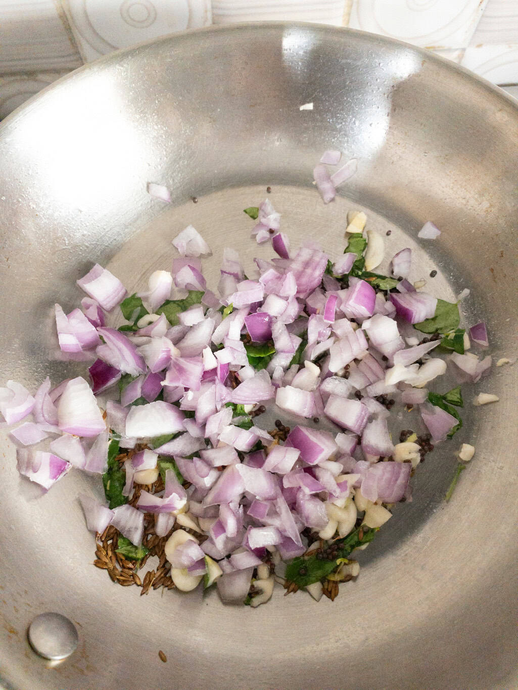 Chopped onions, garlic, curry leaves, mustard seeds, and cumin seeds sautéing in a pan.