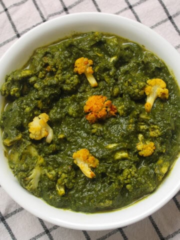Saag gobi served in a white bowl with roasted cauliflower florets in spinach curry.