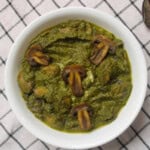 Saag mushroom curry served in a white bowl with mushrooms coated in thick spinach gravy.