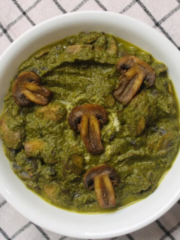 Saag mushroom curry served in a white bowl with mushrooms coated in thick spinach gravy.