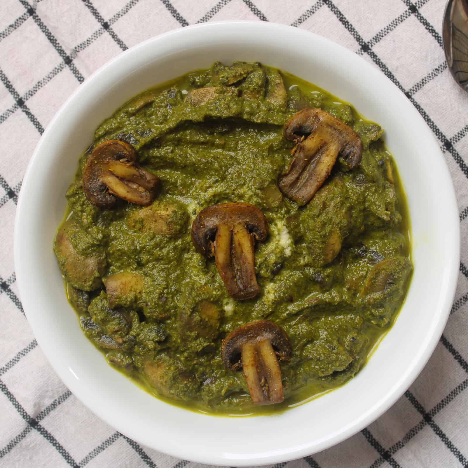 Saag mushroom curry served in a white bowl with mushrooms coated in thick spinach gravy.