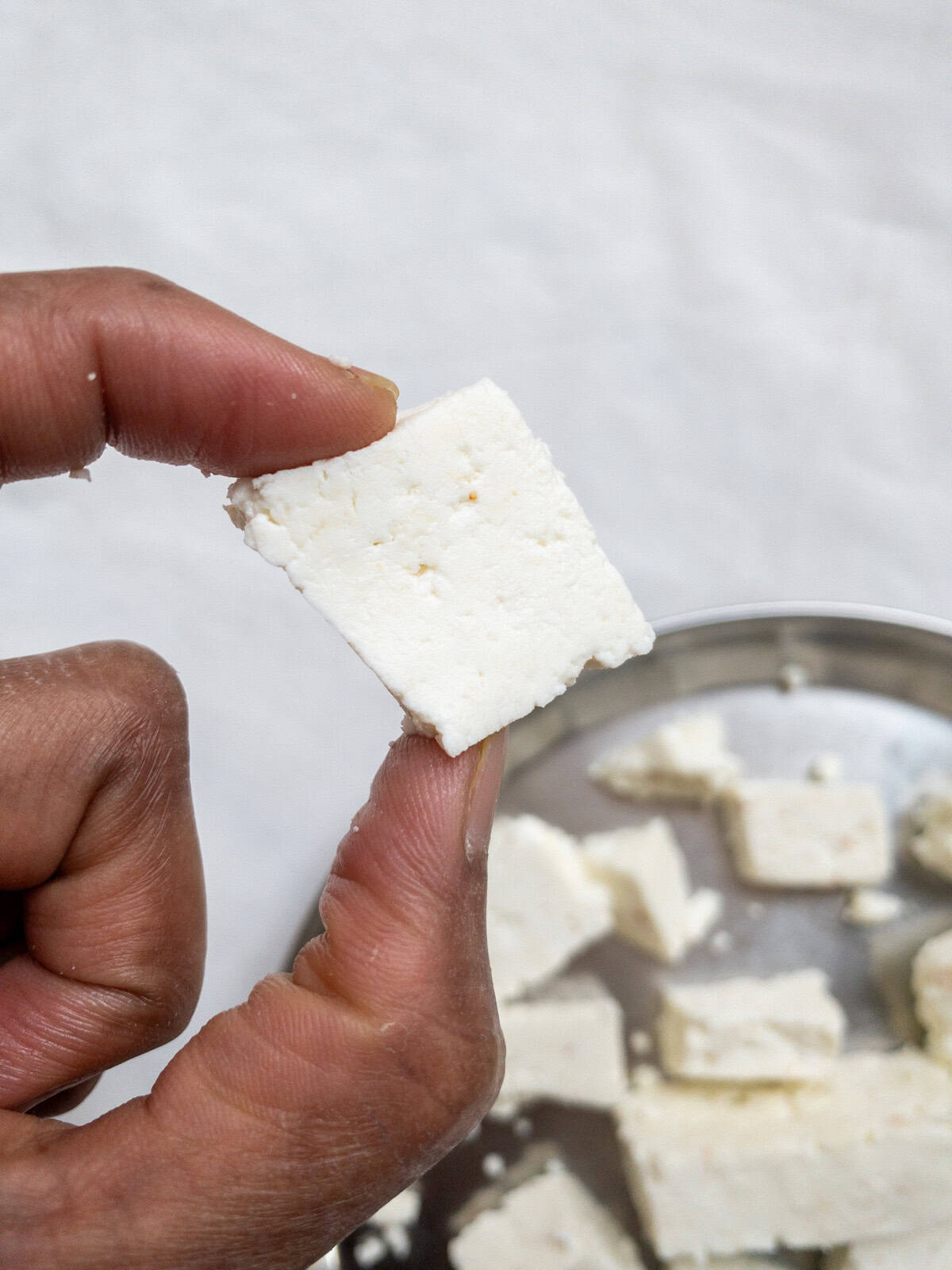 Close-up of fresh homemade paneer cube held by hand.