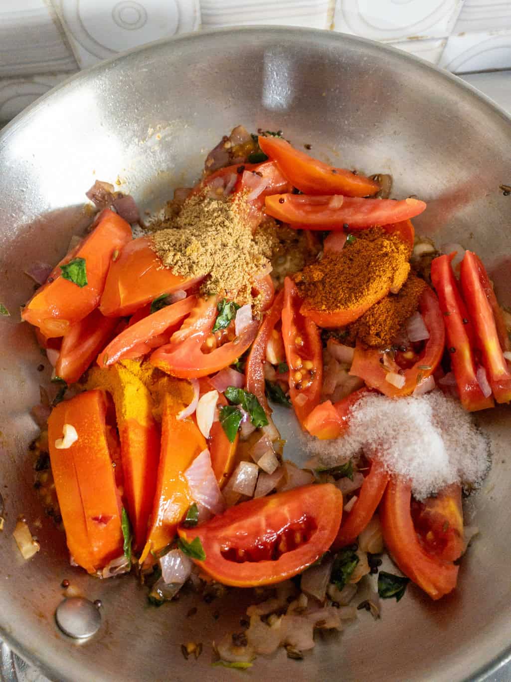 Chopped tomatoes, turmeric, red chili powder, coriander powder, and salt added to sautéed onions for South Indian tomato curry.