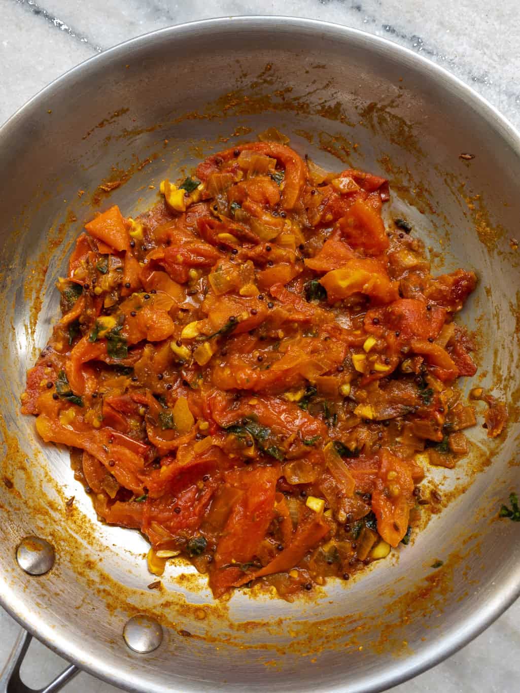 Tomato mixture cooked until soft and slightly glossy with visible mustard seeds and spices.
