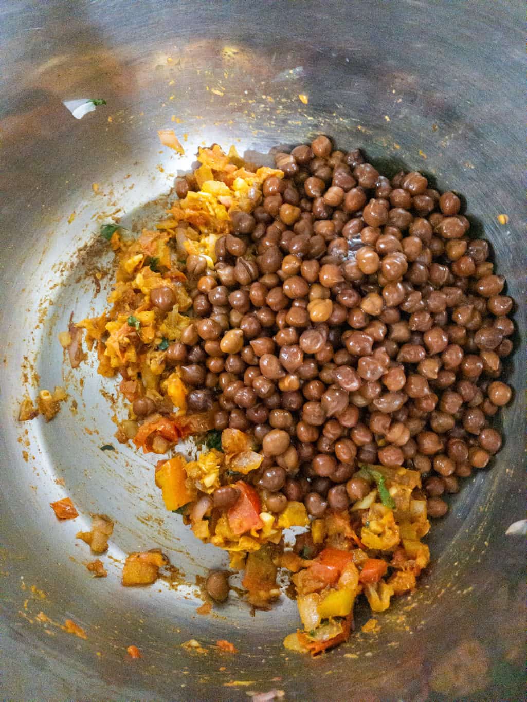 Cooked black chickpeas added to the tomato onion masala in a steel pan.