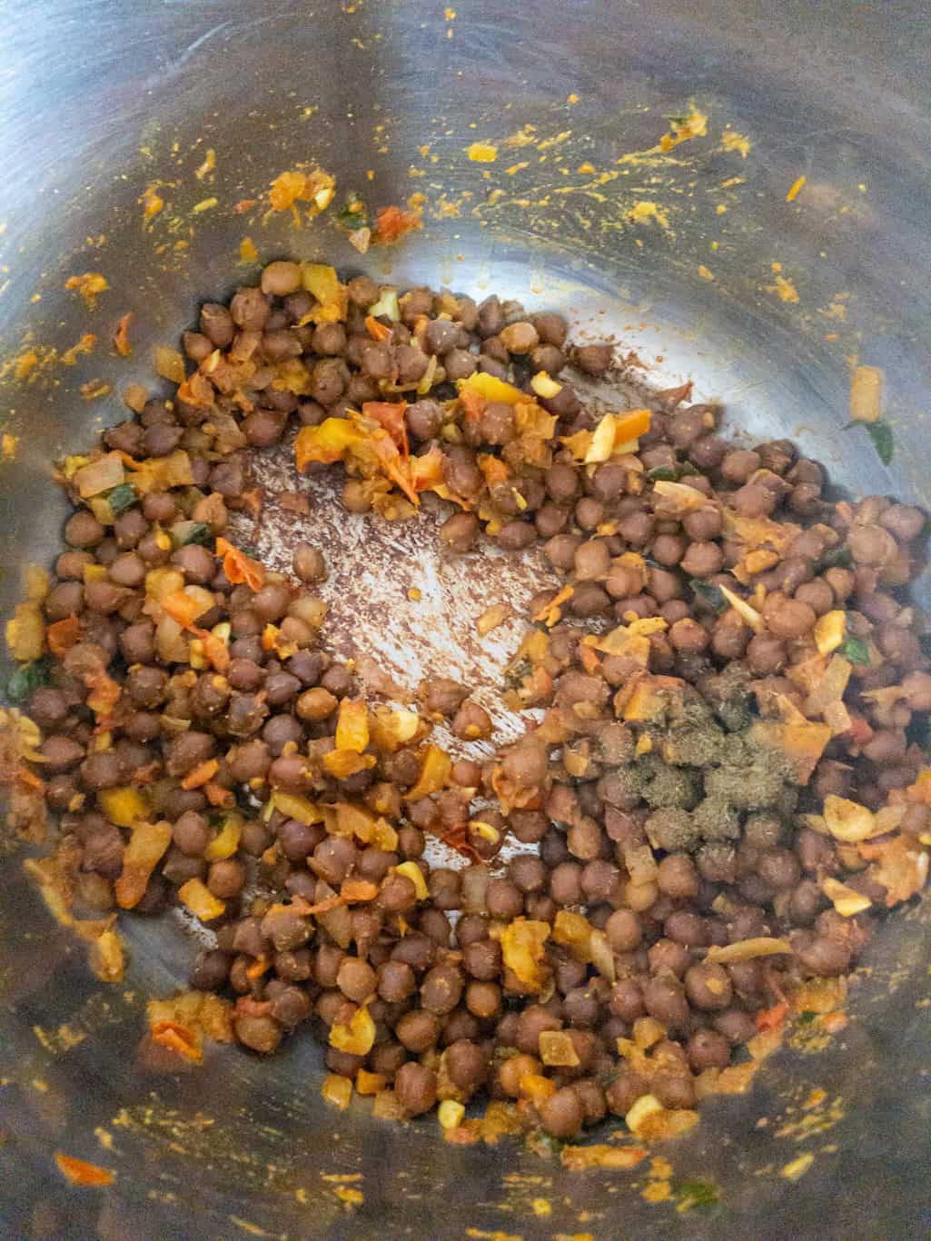 Cooked black chickpeas mixed with masala and final spices in a steel pan.