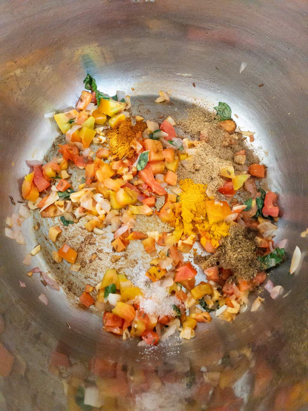 Spice powders and salt added to softened tomato and onion masala in a steel pan.