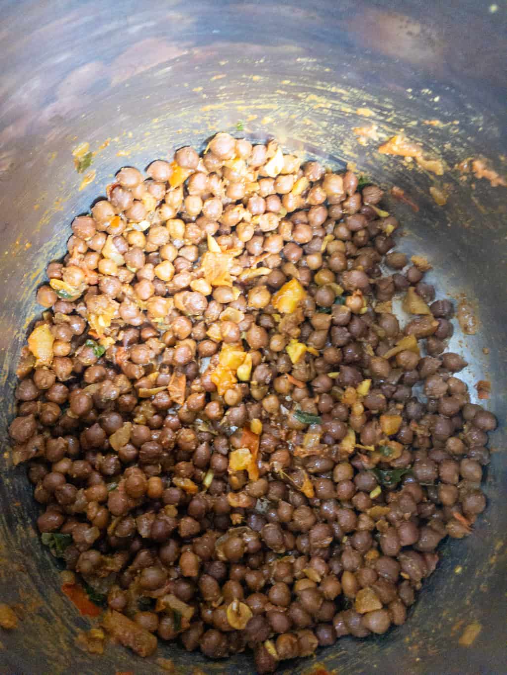 Black chickpeas mixed with tomato onion masala and spices in a steel pan.