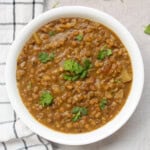 Close view of green moong curry served with coriander leaves in a white bowl.