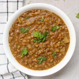 Close view of green moong curry served with coriander leaves in a white bowl.