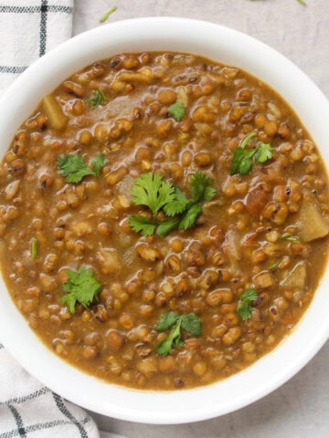 Close view of green moong curry served with coriander leaves in a white bowl.
