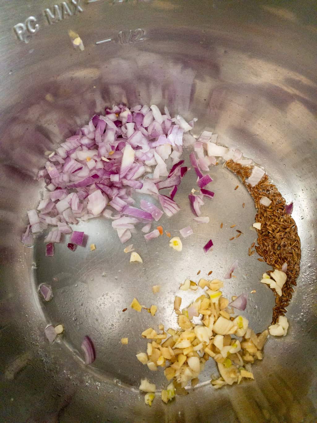 Chopped red onion, minced ginger, and garlic added to the Instant Pot with cumin seeds.