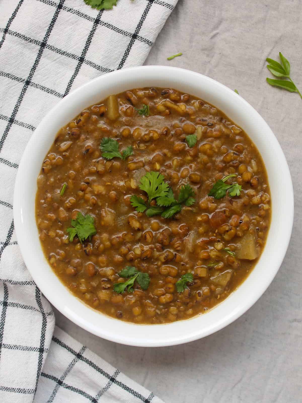 Whole moong dal served in a white bowl with fresh coriander leaves.