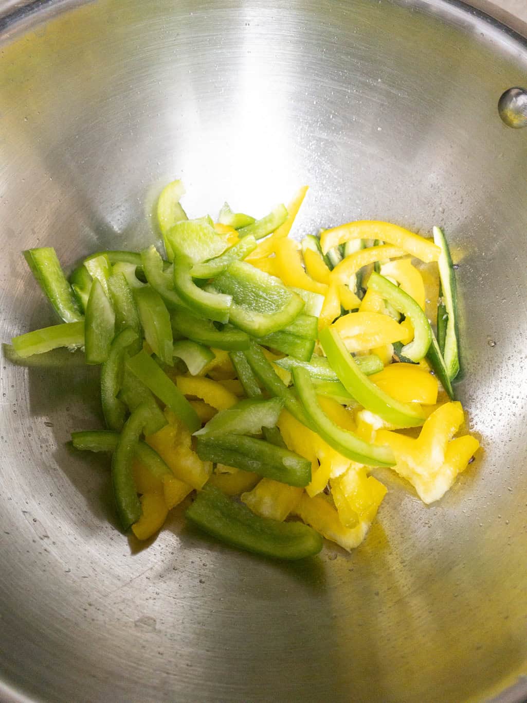 Sliced green and yellow bell peppers in a steel pan.