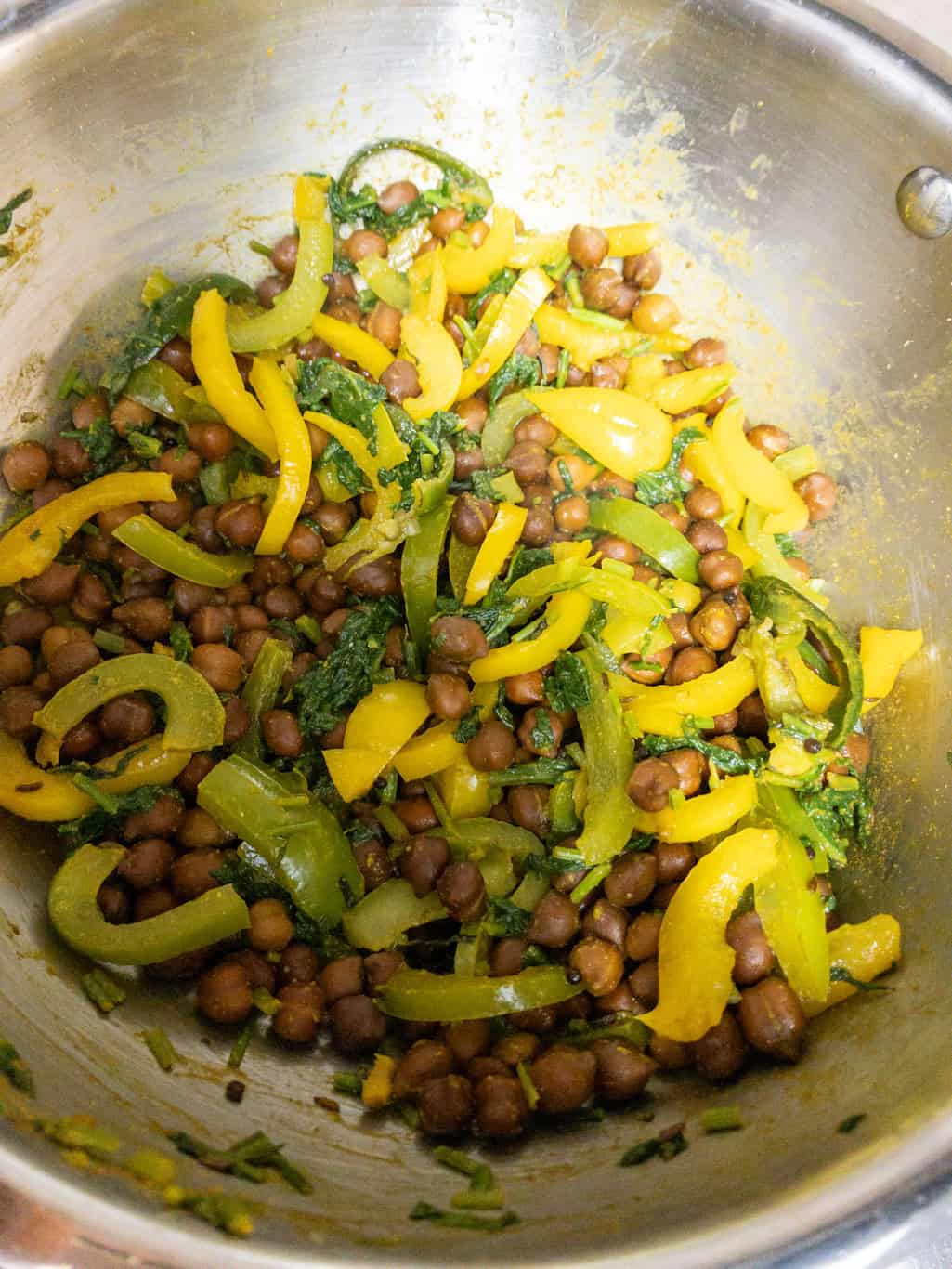 Mixed kala chana curry with bell peppers and spinach in a pan.