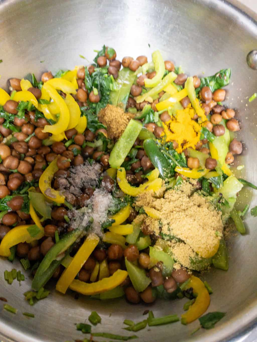 Black chickpeas, bell peppers, spinach, and spices in a pan.