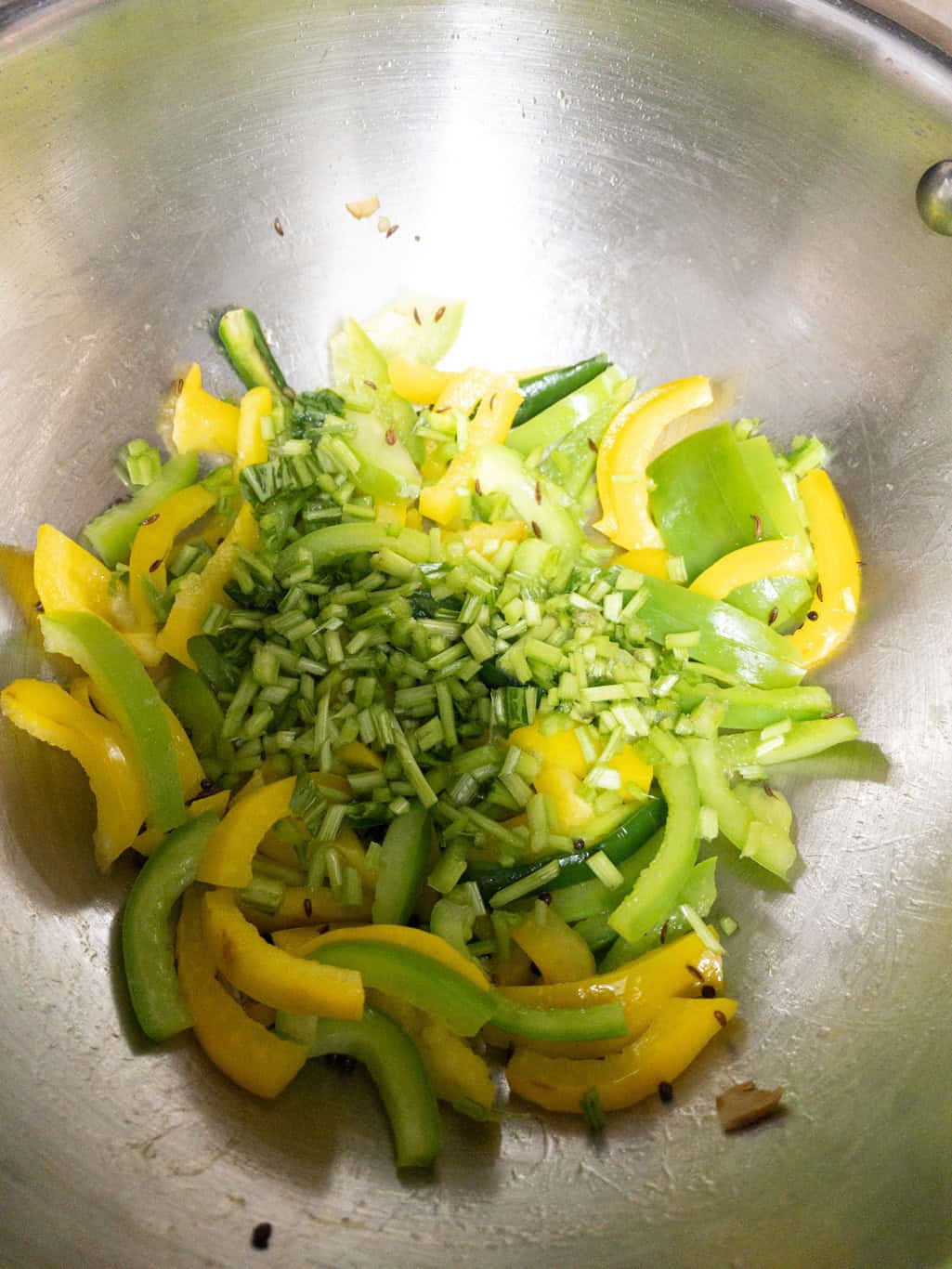 Bell peppers cooking with chopped spinach stems and spices in a pan.