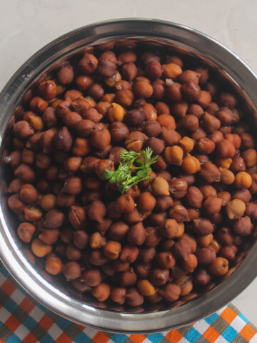 Cooked brown chickpeas served in a steel bowl with fresh cilantro on top.