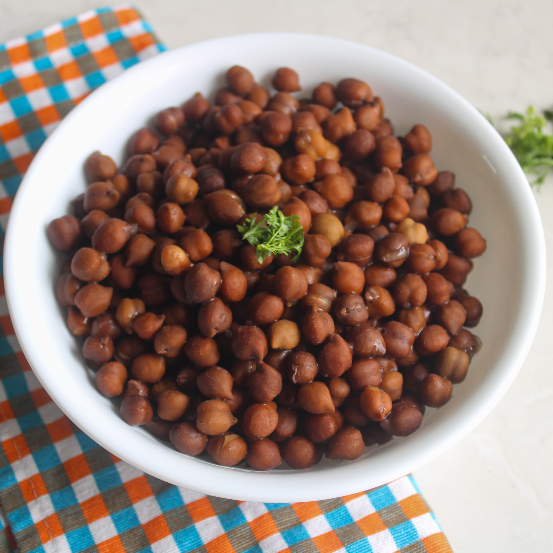 Cooked brown chickpeas served in a white bowl with a small cilantro garnish.