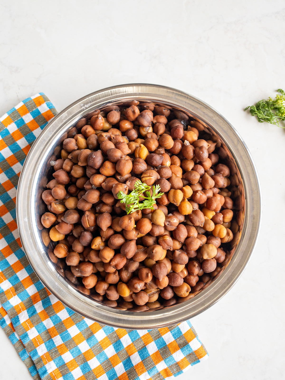 Cooked brown chickpeas served in a steel bowl with cilantro garnish and checkered cloth.