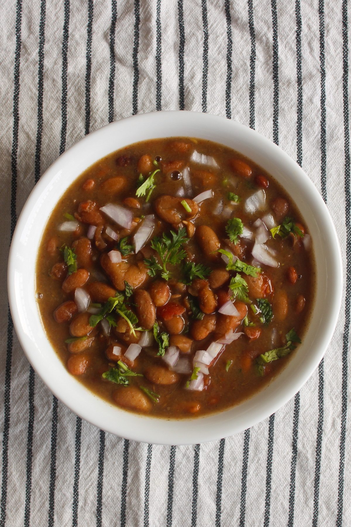 Instant Pot rajma masala in a white bowl with soft kidney beans and onion cilantro garnish.