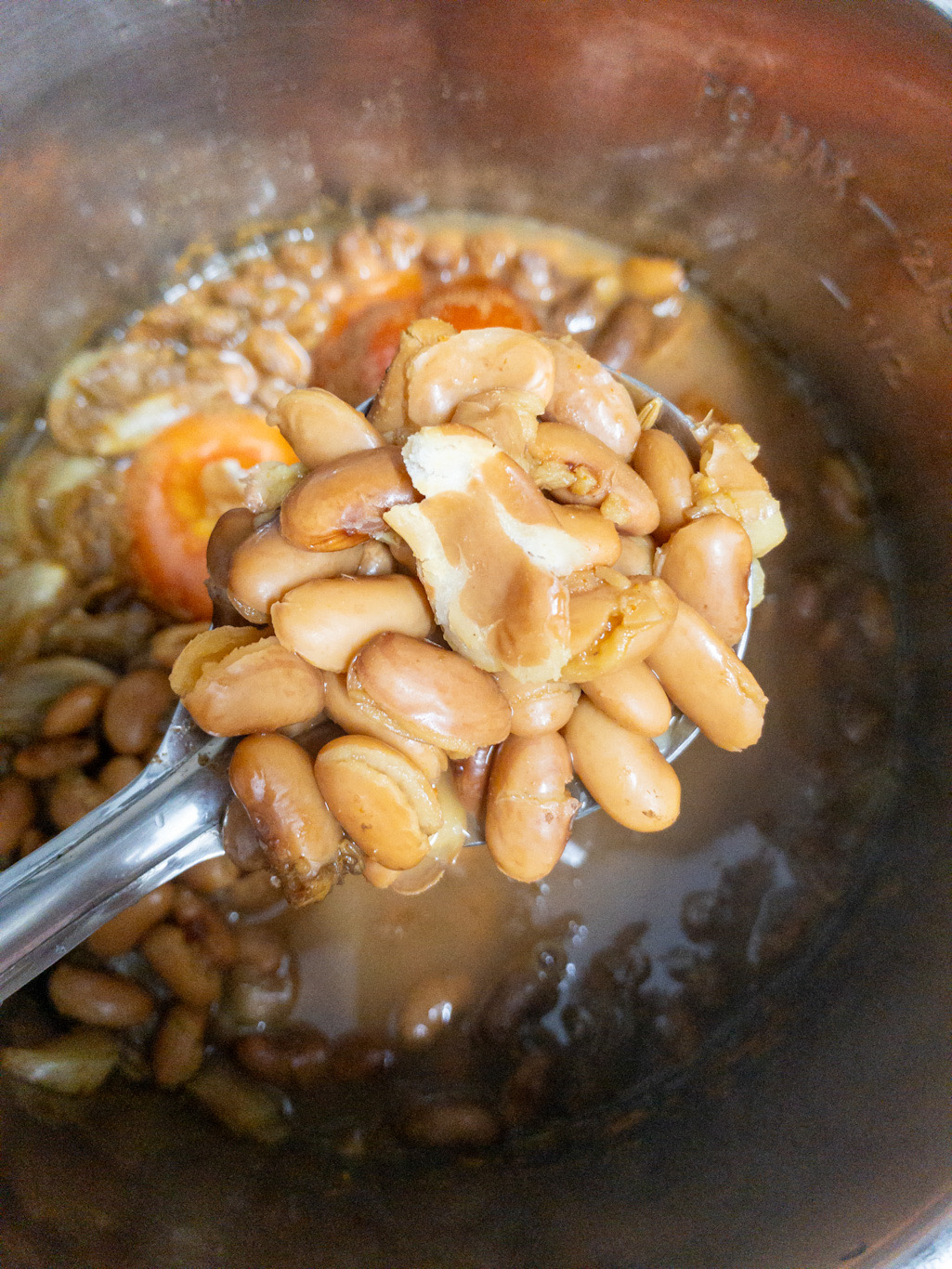 Soft cooked kidney beans are held on a spoon to check doneness after pressure cooking.