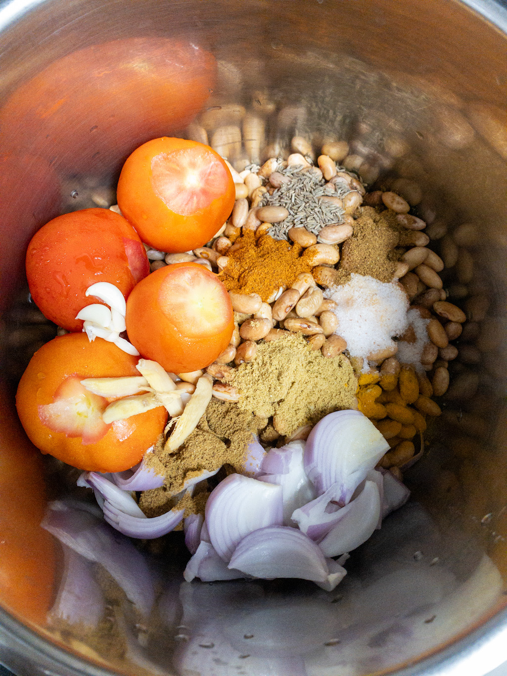 Tomatoes, onions, ginger, garlic, cumin, and spice powders are added over soaked kidney beans.