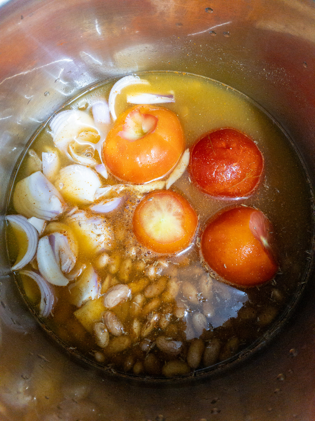 Water is added to kidney beans, tomatoes, onions, ginger, garlic, and spices in the Instant Pot.