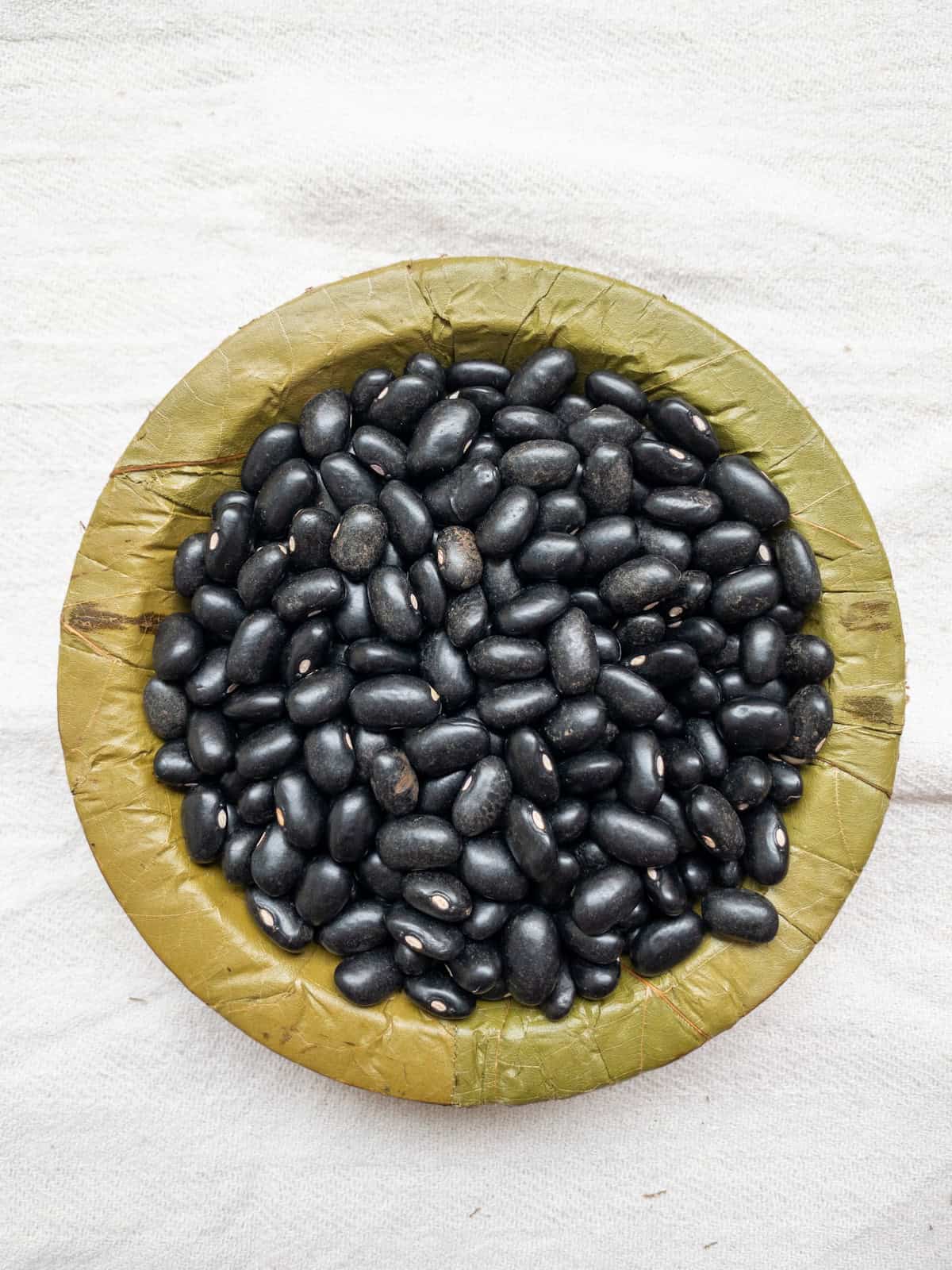 Black beans in a leaf bowl on a white cloth.
