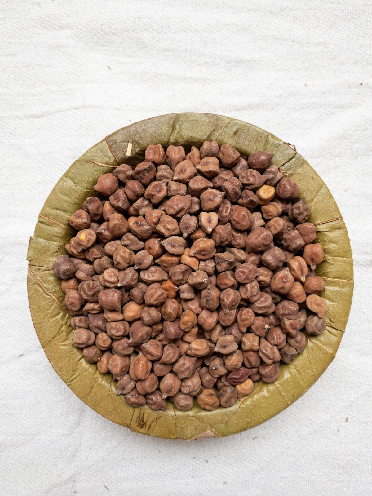 Black chickpeas in a leaf bowl on a white cloth.
