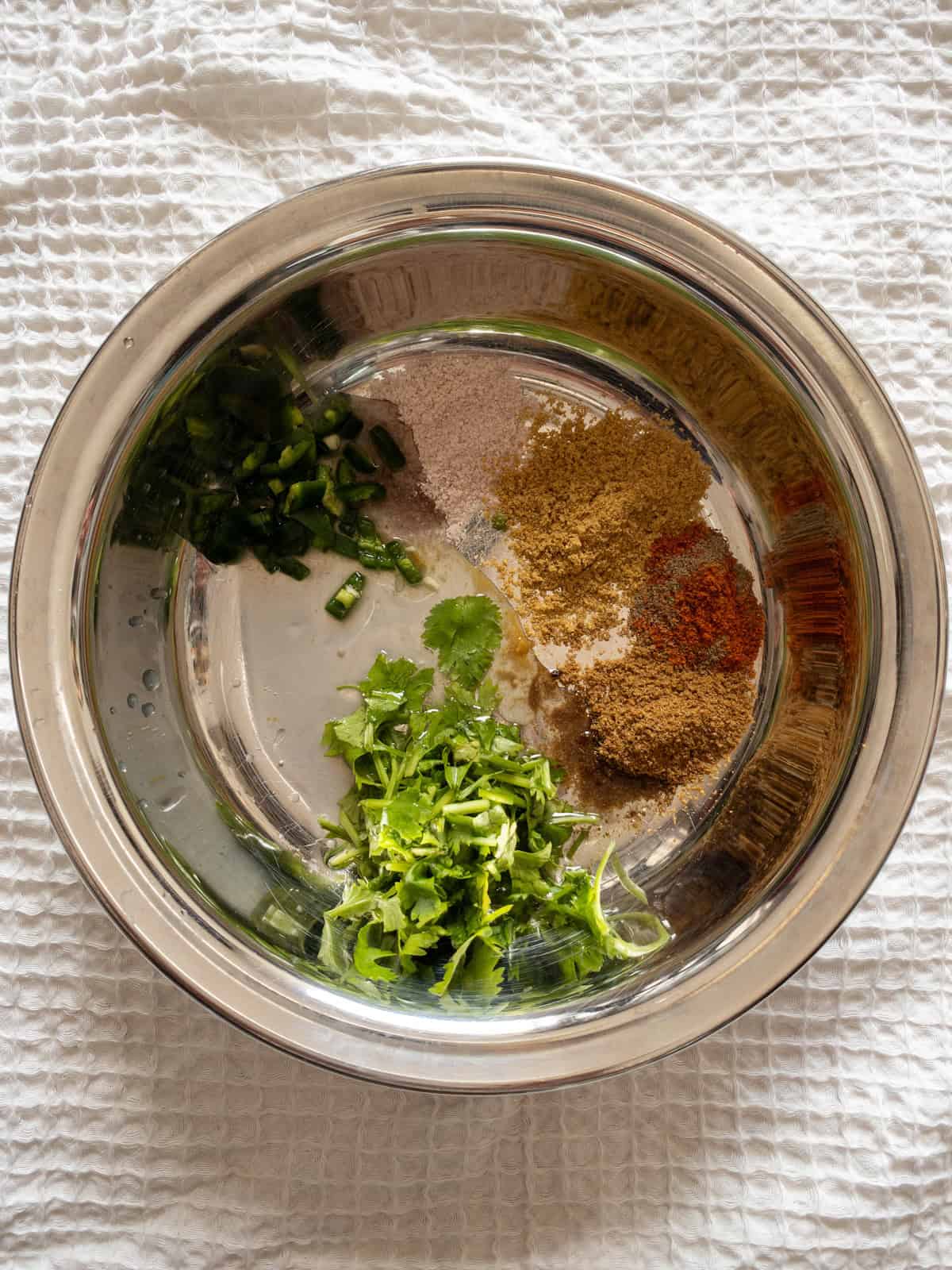 Lemon juice, green chili, coriander leaves, black salt, and ground spices arranged in a stainless steel bowl.